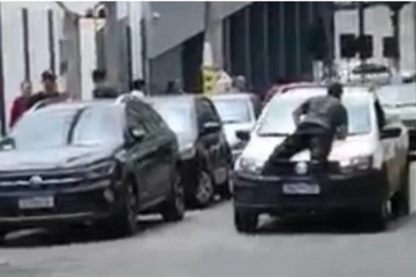 Imagem mostra o momento em que um homem se joga no capo de um carro em movimento - Metrópoles