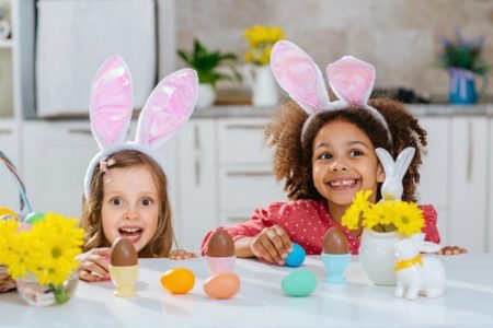 Imagem colorida: duas meninas com orelhas de coelho comendo ovos de chocolate