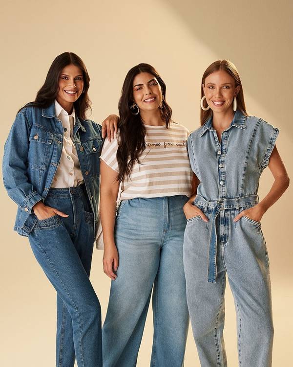 Trio de modelos posando para editorial de moda. Elas estão usando peças jeans - Metrópoles