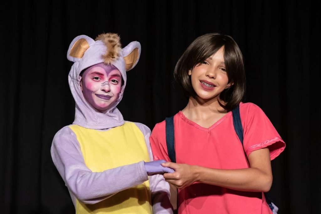 menina de peruca de cabelo curta e pessoa vestida de macaco posam de maos dadas - metrópoles