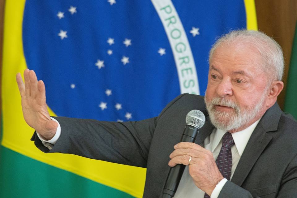 Imagem colorida do presidente Lula discursando em frente a uma bandeira do Brasil
