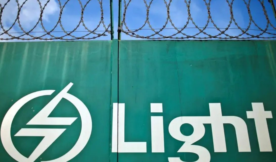 Imagem de muro verde com logtipo da Light na cor de branco. Acima, arame farpado sobre o muro e, ao fundo, o céu azul