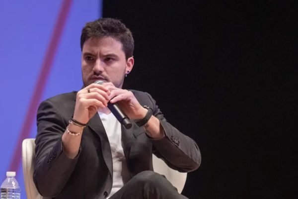 Felipe Neto de terno cinza e camiseta sentado falando em microfone - metrópoles