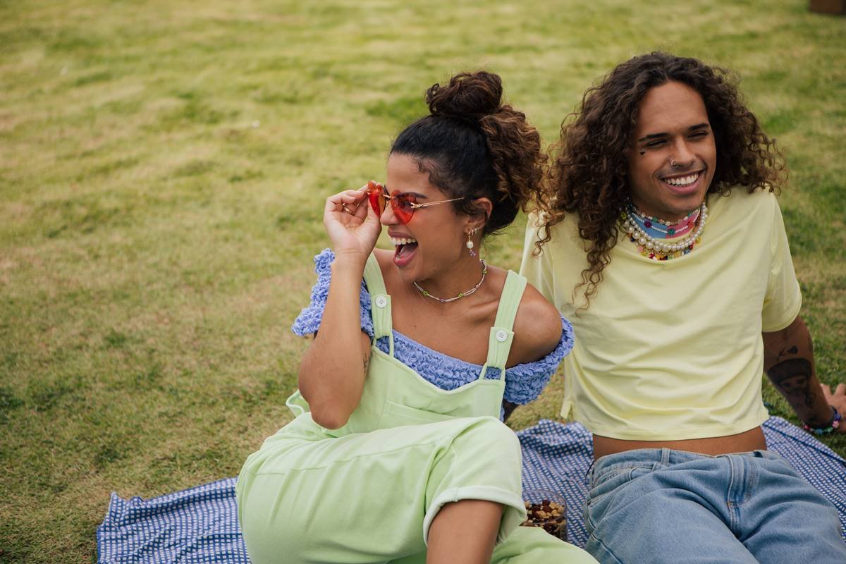 homem e mulher sorriem sentados em pano na grama - metrópoles