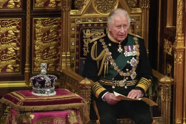 Foto colorida de homem idoso sentado em um trono dourado ao lado de uma coroa - Metrópoles