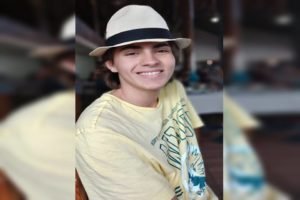 Jovem vestido de camisa amarela e chapéu, sorrindo