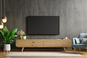 Sala de tv com a televisão na parede, rack com um tapete claro e flores no ambiente