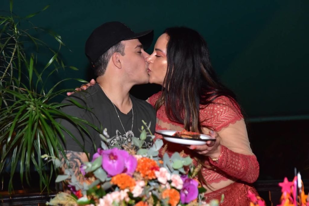 Silvia Abravanel beijando noivo enquanto segura prato com pedaço de bolo - metrópoles