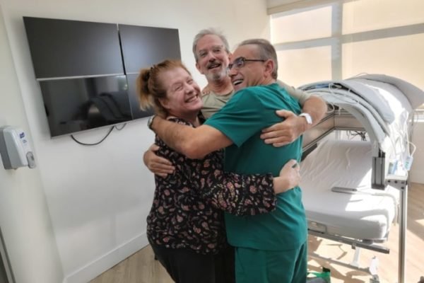 Scott Miller e sua esposa sáo abraçados pelo médico Marc Abreu - Metrópoles