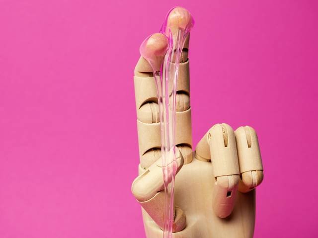 Mão de madeira com lubrificante nos dedos em um fundo rosa- Metrópoles