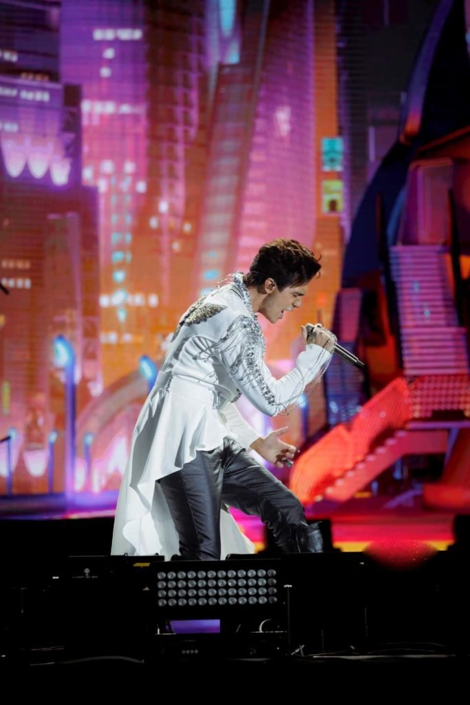 Foto colorida de Luan Santana em gravação de DVD usando roupa branca e cantando - Metrópoles