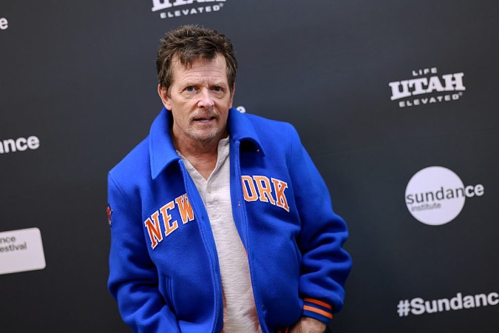 Imagem colorida: ator Michael J. Fox em pé com casaco azul - Metrópoles