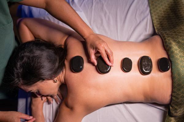 Fotografia colorida mostrando massagem com pedras nas costas de uma mulher-Metrópoles