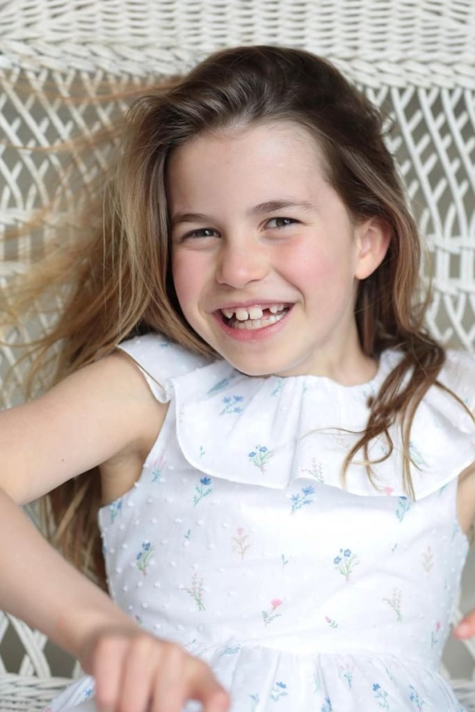 Foto colorida de menina branca, loira, sorridente deitada em uma trama - Metrópoles