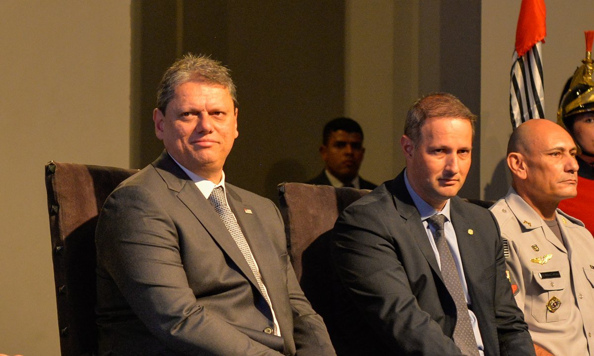 Imagem colorida do governador de São Paulo Tarcísio de Freitas sentado ao lado do secretário de Segurança Pública Guilherme Derrite. Os dois estão vestidos de terno e gravata