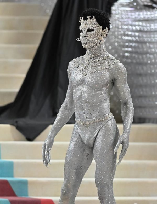 Na imagem com cor, um homem negro com o corpo todo pintado em prata - Metrópoles