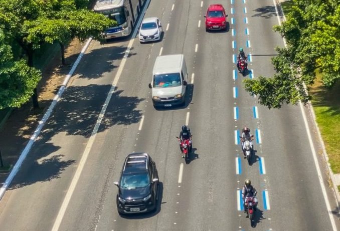 Imagem colorida mostra uma avenida do alto com carros andando em três faixas e, na quarta faixa, pintada na cor azul, andam apenas motos - Metrópoles