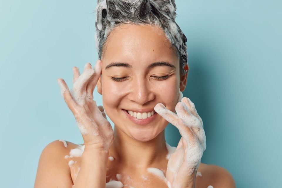 Mulher tomando banho com muito espuma nos cabelos - metrópoles