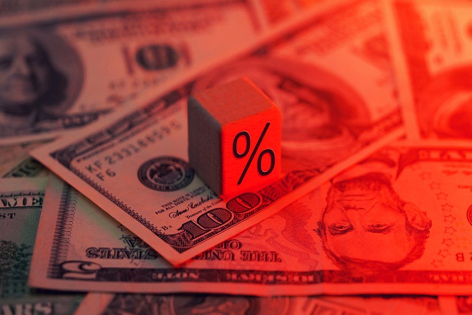 Imagem de notas de dólar sob um dado com o símbolo de porcentagem, iluminadas por uma luz avermelhada - Metrópoles
