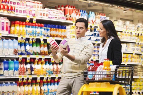 foto colorida de duas pessoas olhando o rótulo de dois produtos em uma seção no mercado - Metrópoles