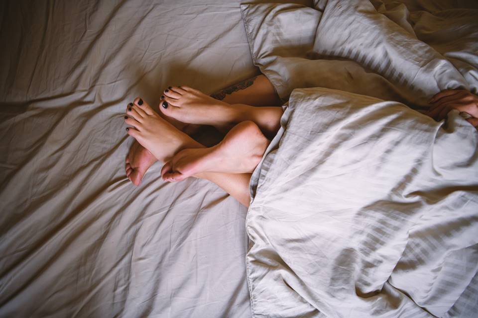 Casal com os pés entrelaçados deitados na cama - Metrópoles