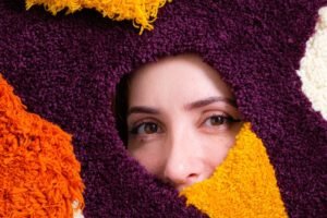 Fotografia colorida mostra os olhos da artista Bruna Zanatta atrás de uma tapeçaria - Metrópoles
