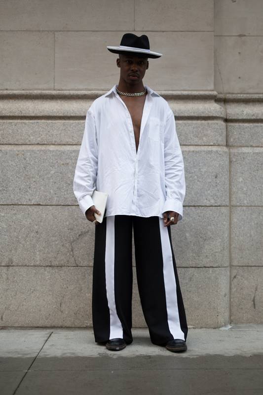 Na imagem com cor, um homem negro usando uma camisa branca e uma calça preta com detalhes brancos - Metrópoles