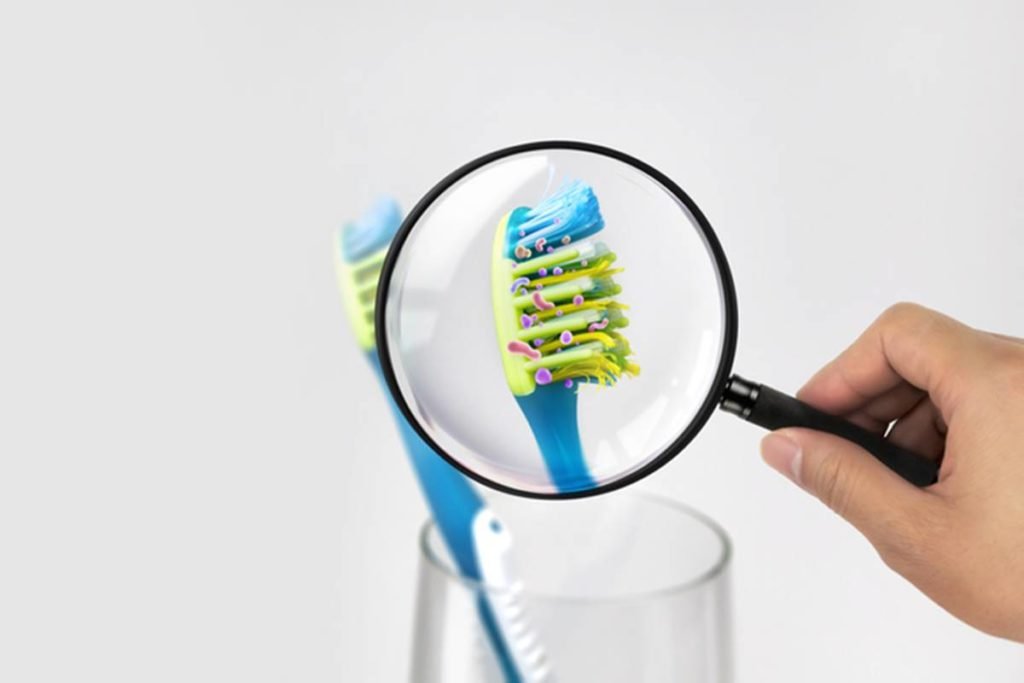 Escova de dentes azul com cerdas verdes sendo vista por meio de lupa que aponta bactérias