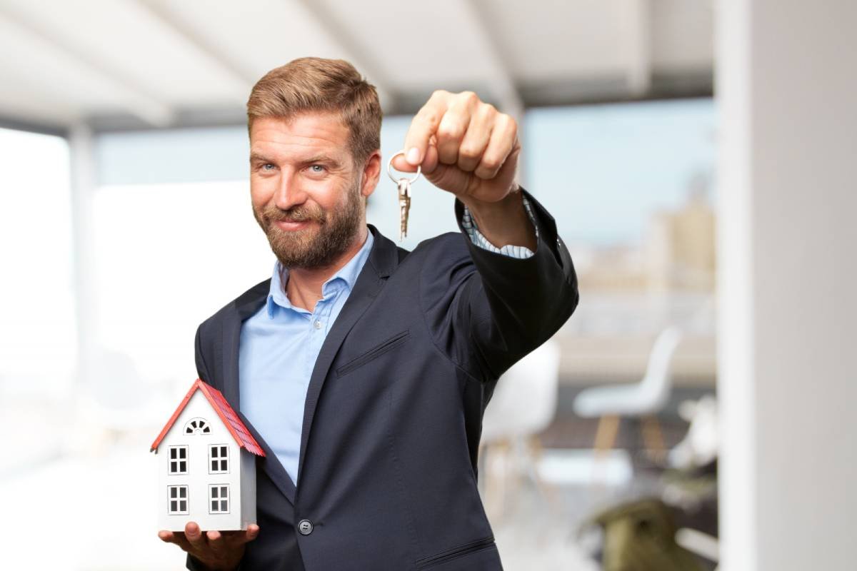 Fotografia colorida mostrando homem de barba com terno segurando chave em uma mão e miniatura de casa na outra-Metrópoles