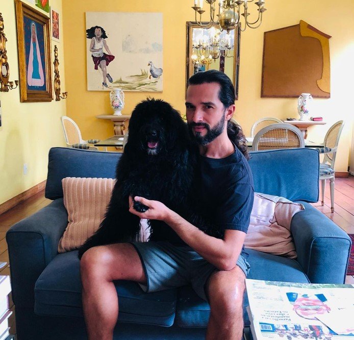 Na foto, um homem sentado em um sofá com um cachorro preto - Metrópoles