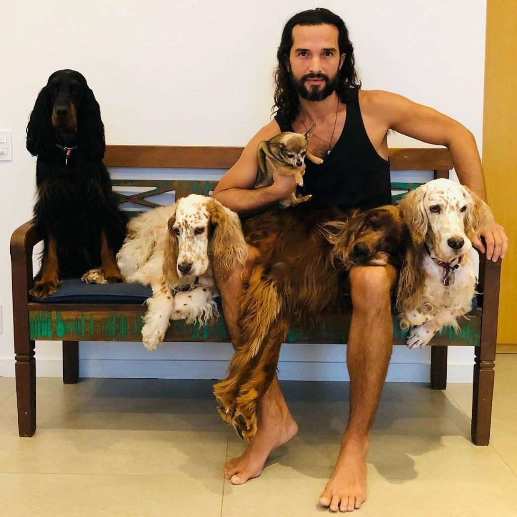 Na foto, um homem sentado em um banco de madeira, cercado por quatro cachorros - Metrópoles