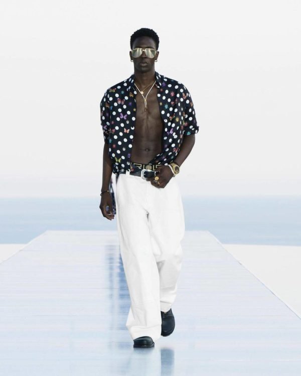 Na imagem com cor, um homem negro usando uma camisa de poá aberta e uma calça branca desfilando - Metrópoles