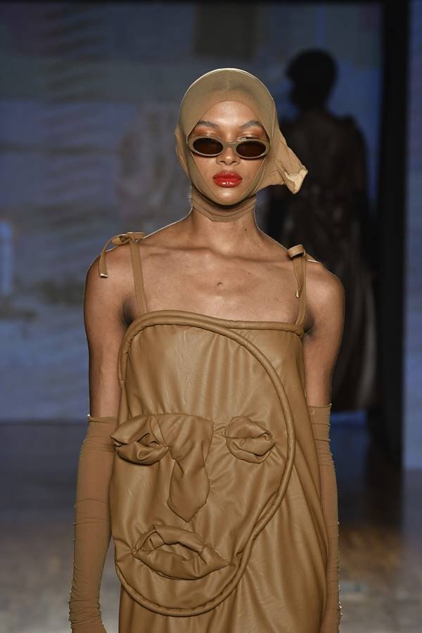 Em desfile, modelo usa meia como touca e vestido marrom com forma de rosto humano - Metrópoles