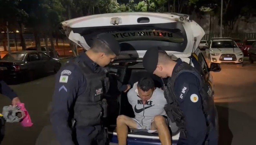 Homem de casaco cinza é levado por policiais. Ele é tirado de camburão