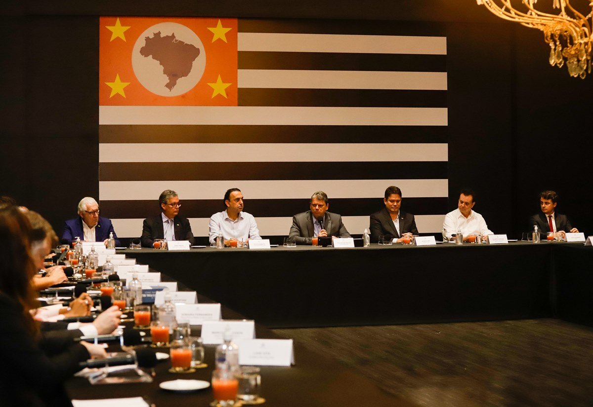 Imagem colorida da reunião de secretários do governo Tarcísio de Freitas no Palácio dos bandeirantes, com a bandeira do estado de são paulo ao fundo - metrópoles