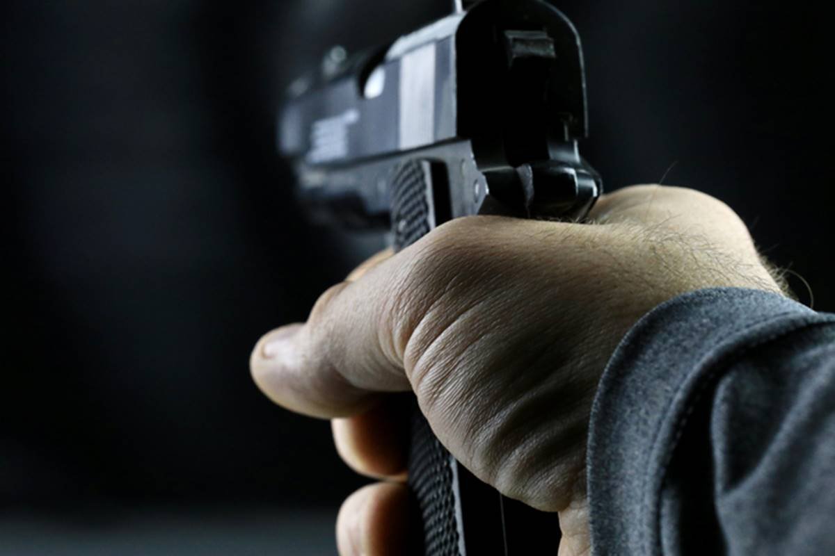 Imagem colorida de uma mão de uma pessoa branca segurando uma pistola