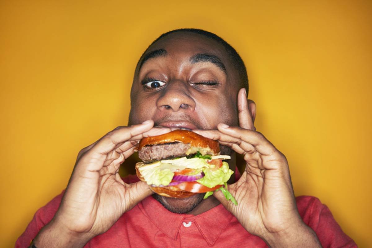 Mastigar pouco: foto colorida de jovem engolindo hamburguer