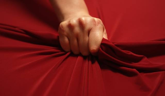 Foto em close de uma mão apertando um lençol vermelho com força - Metrópoles