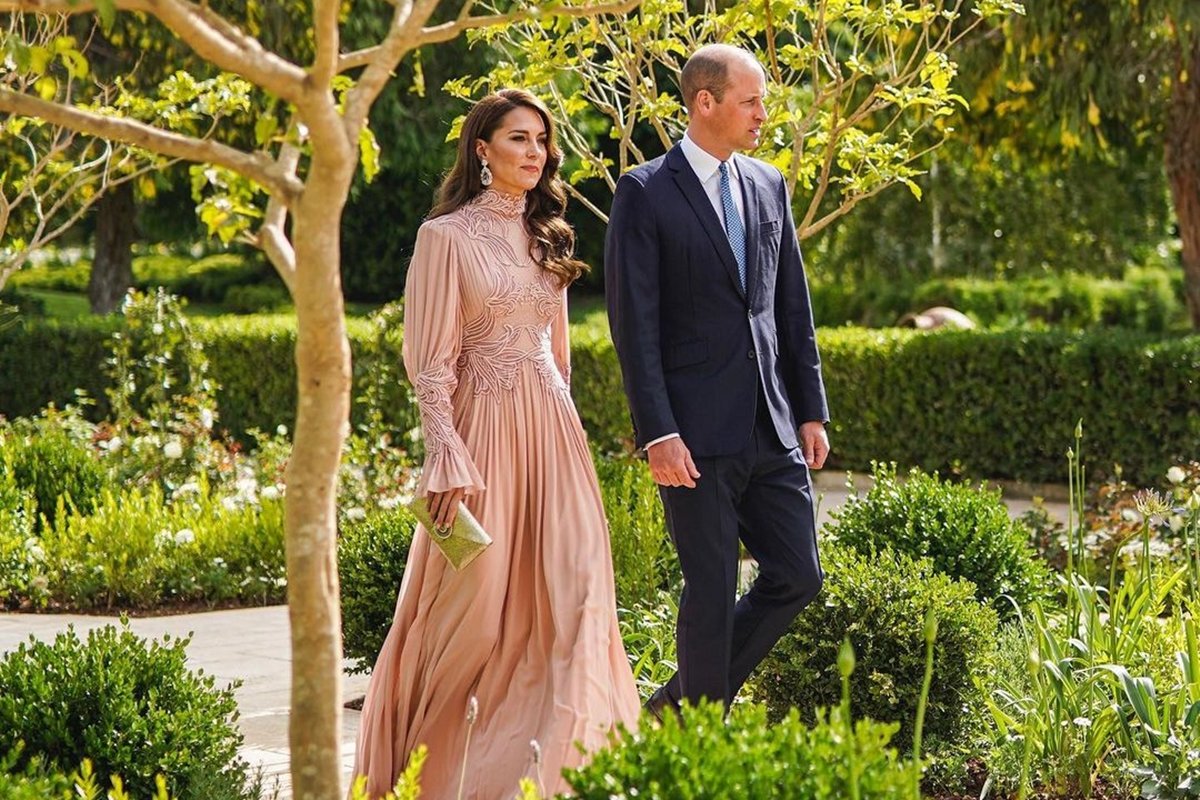 Foto de mulher com vestido no tom rosé e homem com terno. Eles estão andando em meio a um jardim - Metrópoles