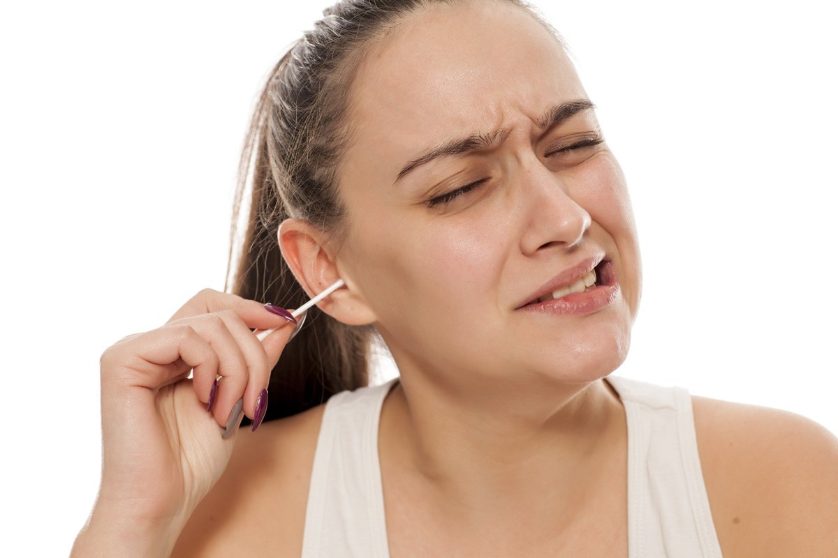 Foto colorida de mulher parda limpando o ouvido com cotonete - Metrópoles