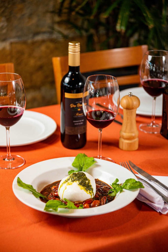Na foto, uma mesa com um prato branco, taça e garrafa de vinho - Metrópoles