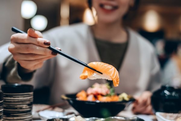 Foto colorida de mulher pegando um sushi com hashi - Metrópoles
