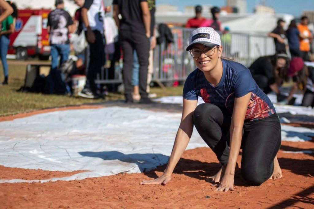 Homem veste boné e camisa azul escura. Ajoelha-se em terra