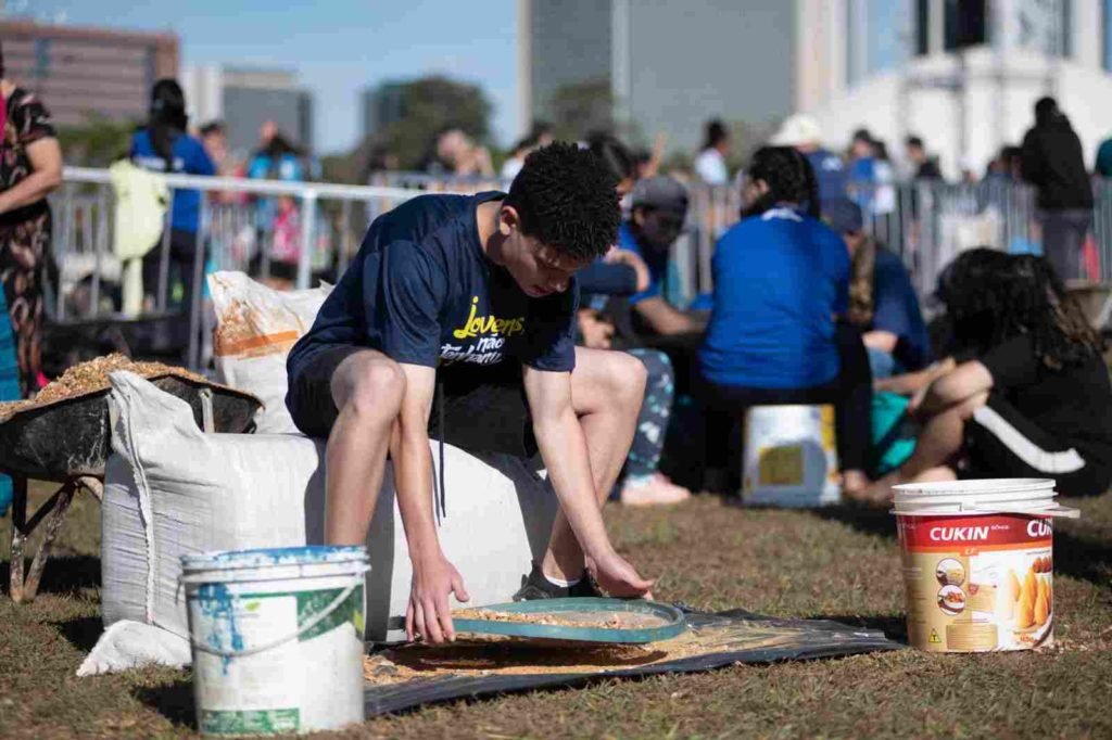Fiel veste camisa azul e ajusta terra em tapete de Corpus Christi