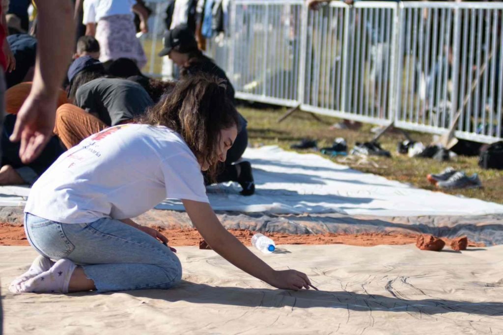 Mulher de cabelos cacheados monta tapete de Corpus Christi em gramado da Esplanada