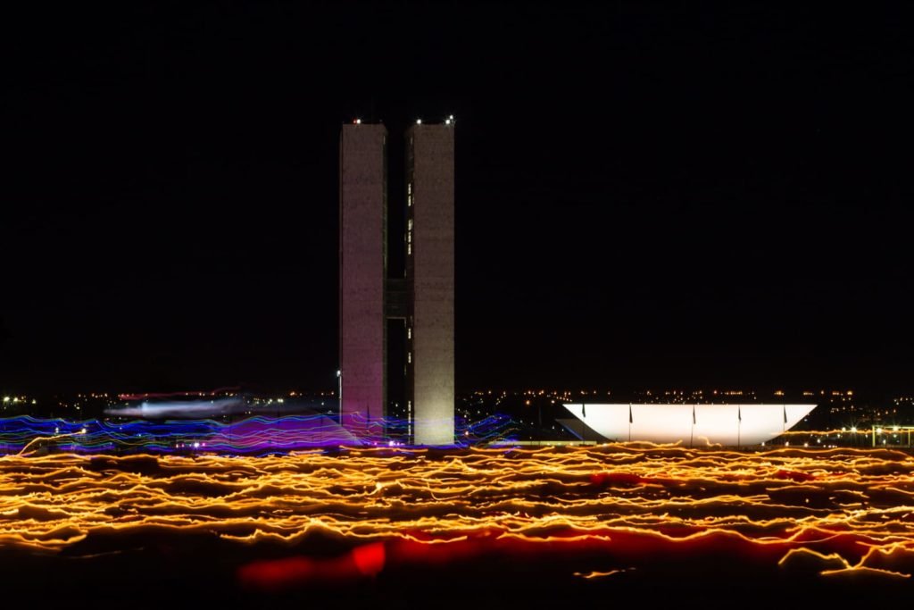 Segurando velas, fiéis participam da procissão com o Santíssimo Sacramento, que percorre o quadrilátero da Esplanada dos Ministérios de frente para a Catedral de Brasília. O Santíssimo Sacramento é transportado no mesmo papamóvel usado na visita do Papa João Paulo II a Brasília.