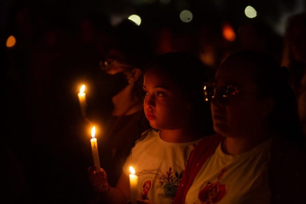 Segurando velas, fiéis participam da procissão com o Santíssimo Sacramento, que percorre o quadrilátero da Esplanada dos Ministérios de frente para a Catedral de Brasília. O Santíssimo Sacramento é transportado no mesmo papamóvel usado na visita do Papa João Paulo II a Brasília.