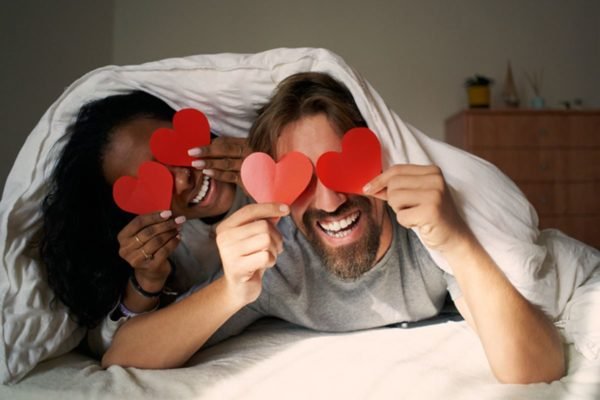 Imagem colorida: mulher e homem seguram corações de papel nos olhos - Metrópoles
