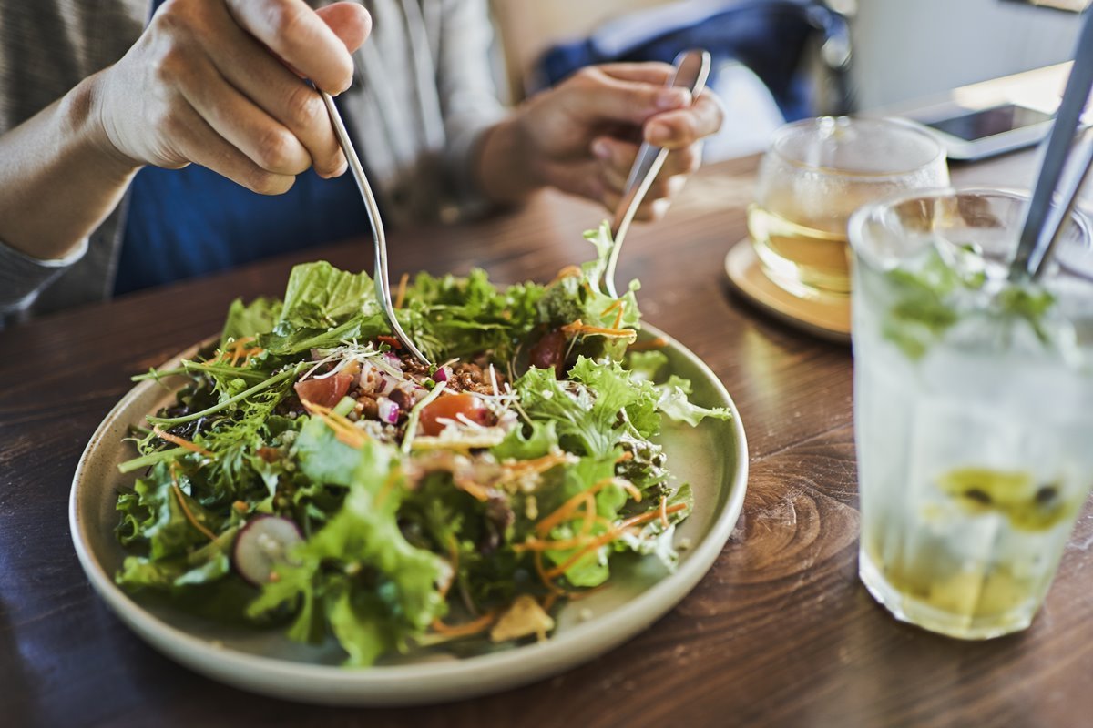 Foto colorida de prato com salada enquanto pessoa pega folhas da hortaliça com um garfo e faca - Metrópoles