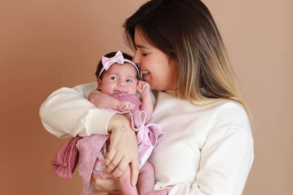 Imagem colorida mostra a influenciadora Viih Tube, que é branca e com o cabelo castanho, cheirando a cabeça de sua filha, uma recém-nascida vestida de rosa - Metrópoles